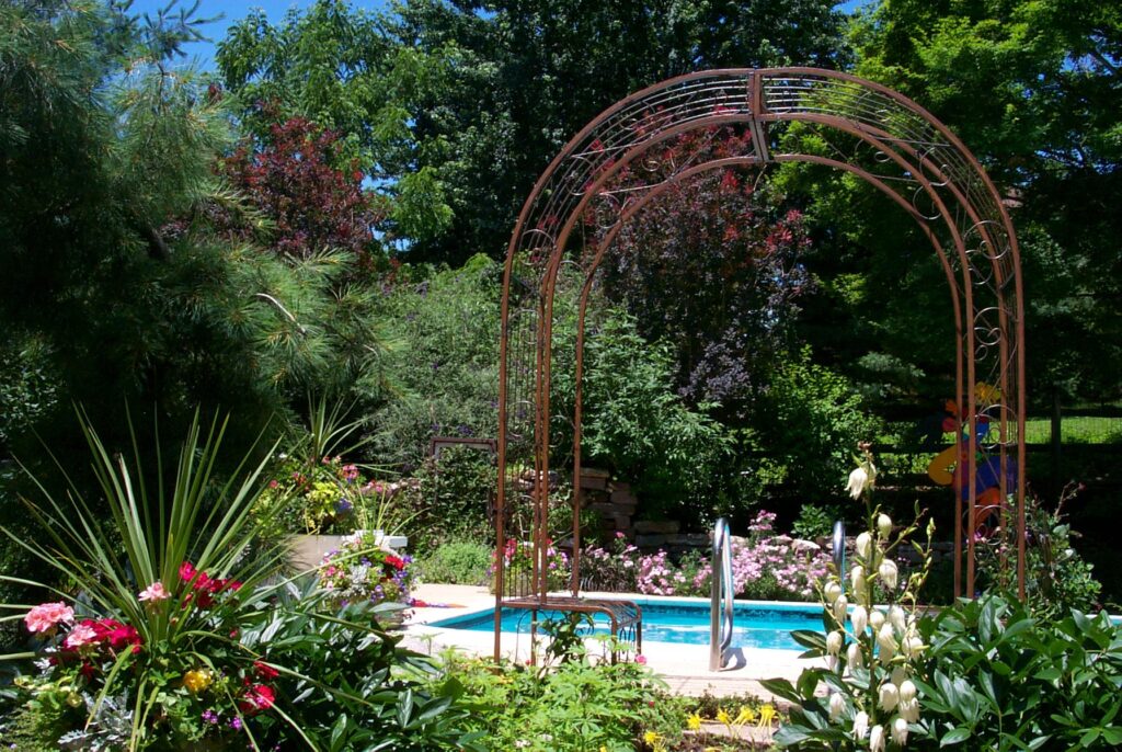 Swimming pool with surrounding gardens, trees, and accent arbor